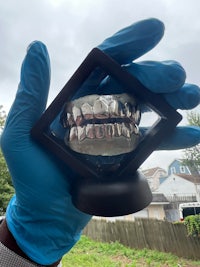 a person holding up a silver gummy grin in a blue glove
